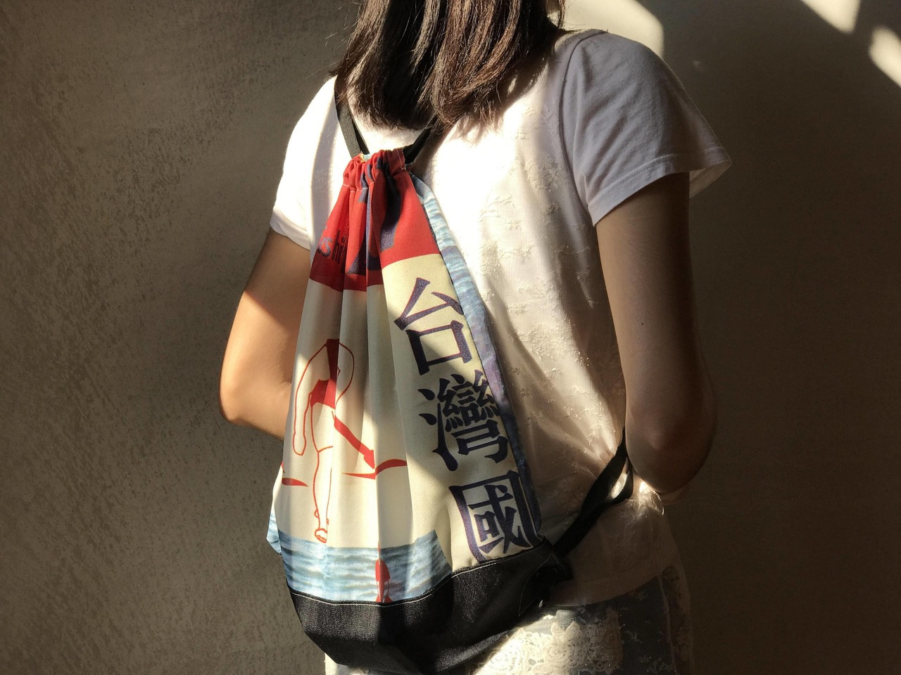 有一個女生背著束口袋，包上頭有台灣國字樣