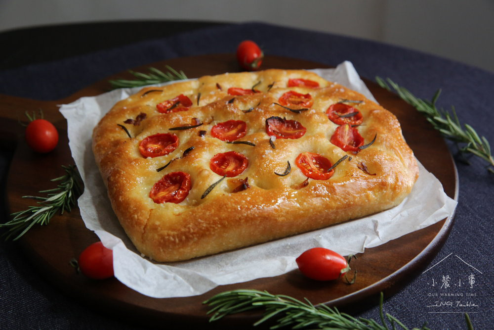 佛卡夏麵包，烤乾的番茄和迷迭香，麵包在烘焙紙上，新鮮的小番茄4顆，圓形木頭砧板